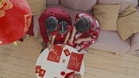 Top view shot of Chinese family of three in traditional clothing sitting on couch at home and making Lunar New Year postcards