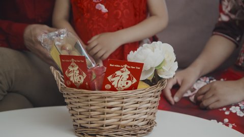 Handheld close up with tilt down of Asian family in traditional red tangzhuang and cheongsam costumes preparing gift basket for Chinese New Year