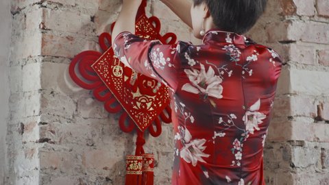 Tracking shot of Asian woman in qipao hanging Chinese New Year decoration on wall