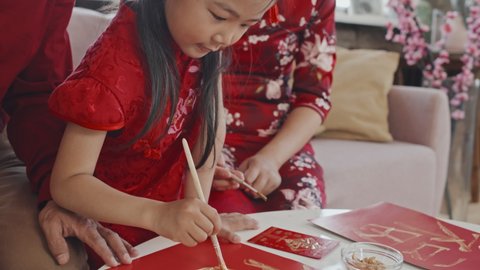 Tilt down close up of cute Asian 5-year-old girl and her parents making Chinese New Year postcards