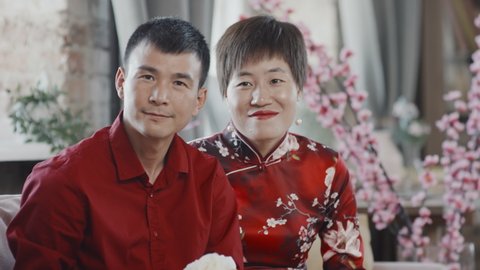 Tilt up portrait of married Asian couple in red shirt and traditional qipao dress holding Chinese New Year gift basket and posing for camera