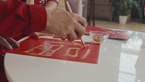 Close up shot of unrecognizable father and daughter painting Chinese character on red sheet of paper and making postcard for Lunar New Year celebration