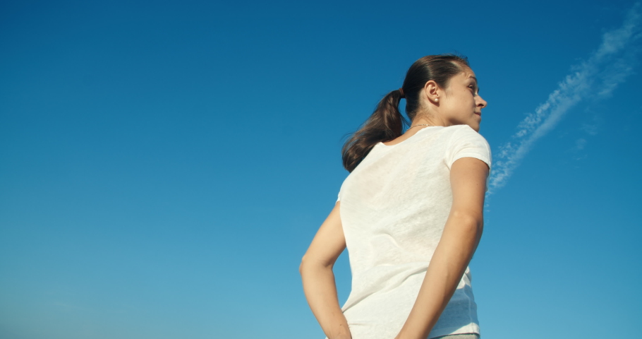 Young adult attractive woman with long brunette hair looking around on blue cloudy sky as background and enjoying of summer windy evening 