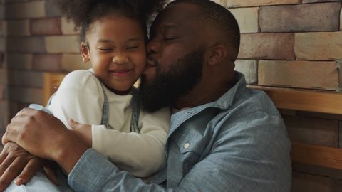 Slow motion. An African American father hugs his cute little kid in bedroom at home. Black Dad kiss daughter forehead. love, family relationship and father day