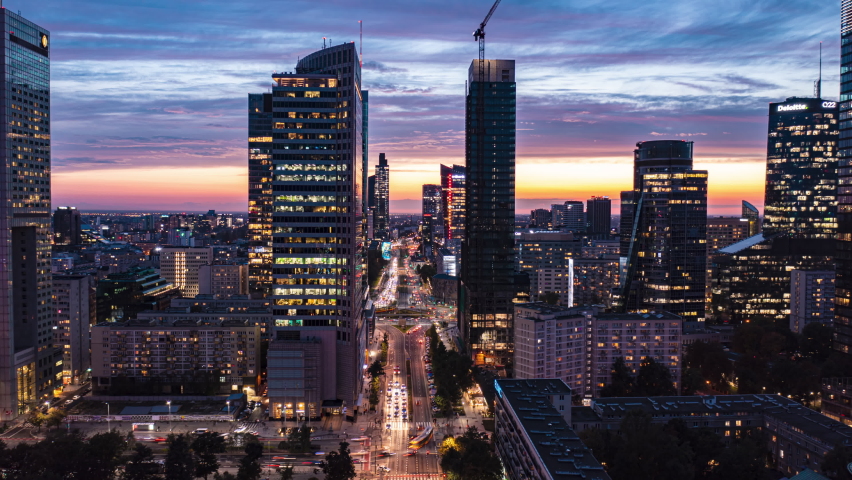 Fly forwards above wide downtown boulevard. Amazing hyperlapse of straight multilane main road leading between modern skyscrapers against sunset sky. Warsaw, Poland