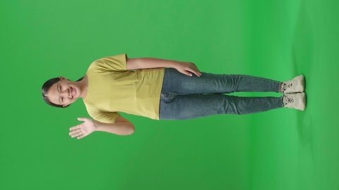 Full Body Of Happy Young Asian Kid Girl Waving Hand And Say Bye Bye While Standing On Green Screen In The Studio
