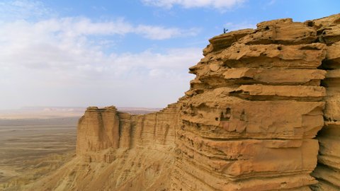 Aerial Panning Over A Woman Standing On The Edge Of A Soaring Cliff In An Arid Desert Under Hazy Skies - Arabian Desert, Saudi Arabia