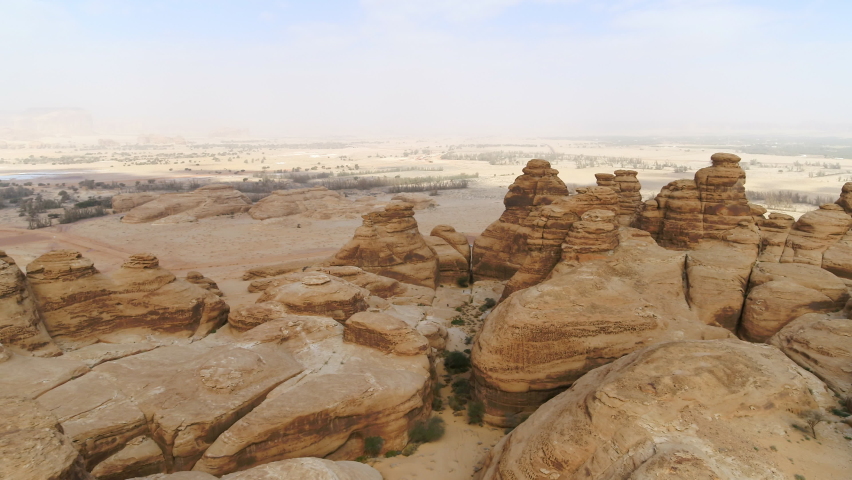 Aerial Moving Forward And Descending Into Eroded Desert Rock Formation With Hazy Skies And Arid Terrain - Arabian Desert, Saudi Arabia Royalty-Free Stock Footage #1081796978