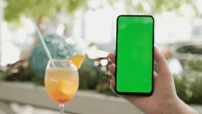 View of female hand holding and pressing on smartphone with mockup green screen in the restaurant european city. Concept of chroma key and greenscreen