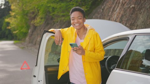 Car breakdown. Young african woman standing on road, contacting auto service online and receiving solution help waiting on road and celebrating victory.