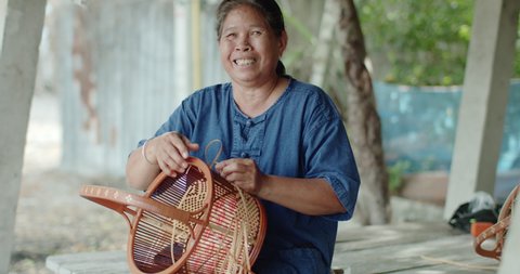 Smiling Thai female farmer weave basket in traditional Thai art patterns to sell as extra income in countryside of Thailand.
