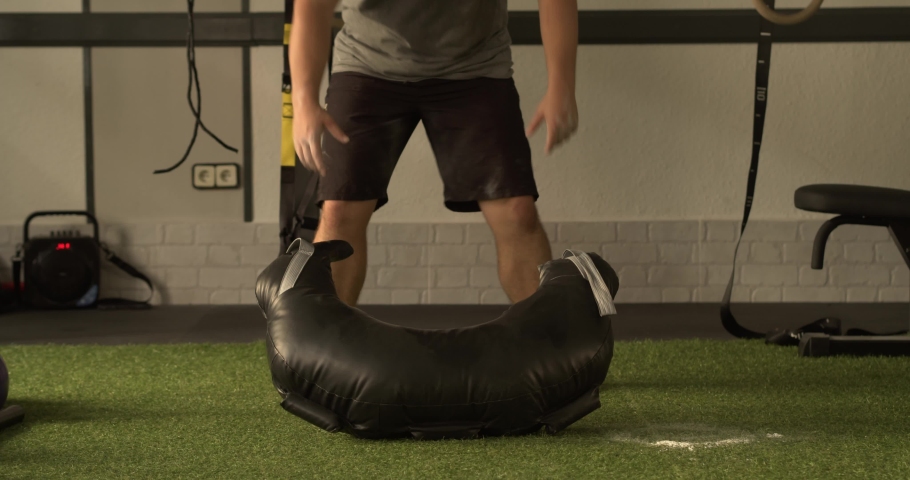 Caucasian man lifts a Bulgarian Training Bagen a strength training in the gym