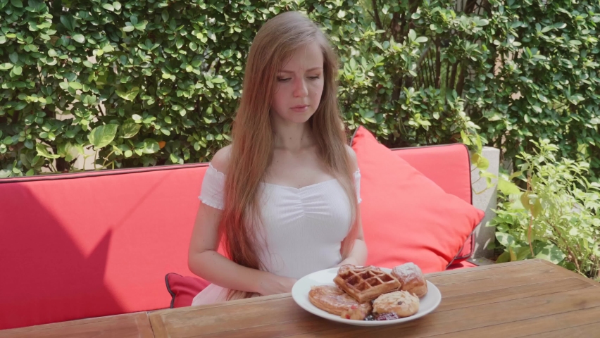 Slim Young Woman on Dieting Aggressively Refuse to Eat Pastry. Angry Beautiful Female Push Out Plate with Bakery. Gluten Intolerance. Girl with Long Hair Don't Want to Eat Sweet Fast Carbohydrates.