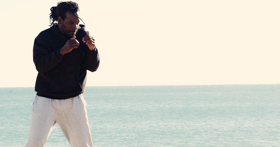 African American fighter man with dreadlocks hair trains martial arts on the beach