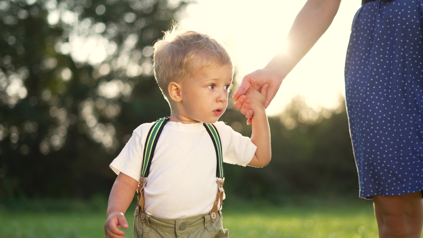 Happy family. Mom holds hand of her son in park. Parent and child in green grass. Family in rays of sun. Happy child holds mom hand. People in natural park. Happy family standing on green grass