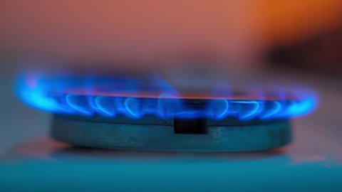 Kitchen burner turning on and turns off at the end of footage. Natural gas inflammation, close up. Stove burner lights up and burns with a blue flame on an orange background.