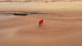 4K video from a drone as a beautiful blonde girl in a red jacket draws a heart on a sandy beach of the Baltic Sea in autumn in gloomy weather.