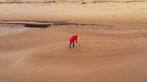 4K video from a drone as a beautiful blonde girl in a red jacket draws a heart on a sandy beach of the Baltic Sea in autumn in gloomy weather.