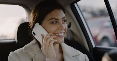 Close Up Slow Motion of Attractive Young Caucasian Woman in Car Using Mobile Phone. Female Brunette on Backseat of Ride Sharing Transportation Talking on Smartphone.