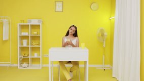 Young lady, manager, office worker, is sitting at office desk in yellow space, using mobile phone, looking for some information and news, creative video, Slow motion.