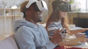 Young joyous multiethnic couple in VR headsets sitting on sofa, using gamepads and playing video game together at home - Powered by Shutterstock - Get 15% off with code: PIKWIZARD15