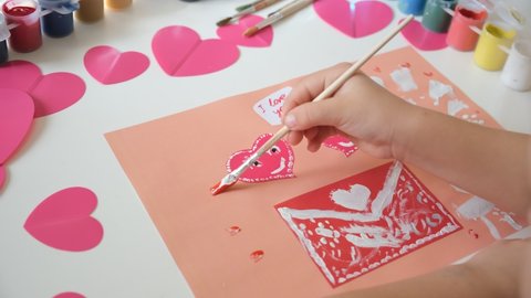 Child making homemade greeting card. A little girl painting and coloring card with funny hearts. Gift for Mothers Day or Valentines day. Arts and crafts concept.