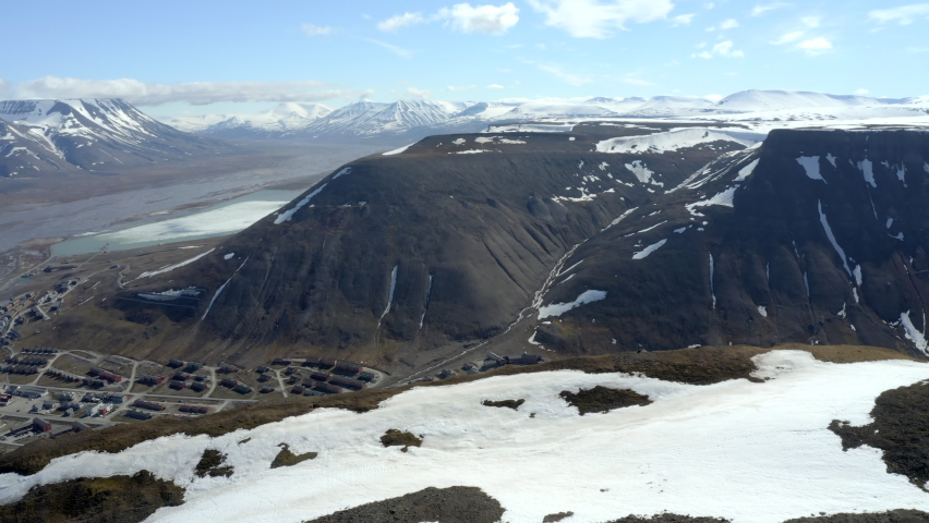 Sliding shoot - city reveal. Norway - Longyearbyen. Svalbard. Sliding left, panning down. Snow covered mountains. Arctic landscape.