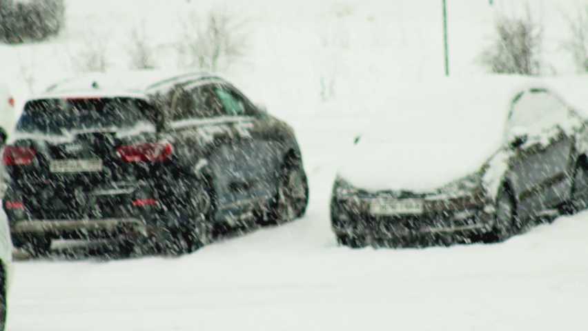 Cars covered with snow in a parking lot in the city during a snowfall. Snow flakes on the background of cars, parked