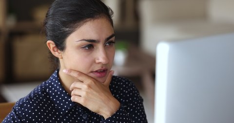 Smiling inspired young Indian female freelancer sit by computer enjoy working process create startup develop software code. Happy millennial lady journalist full of good new ideas write article on pc
