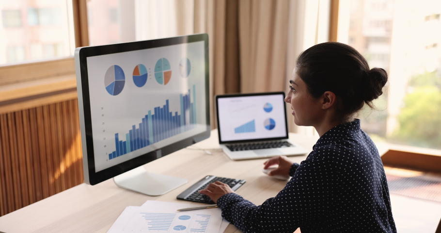 Smiling Indian woman statistician analyze market segments using sales statistics performed in infographic. Young lady trade expert use convenient app to work with data on pc at home office workplace | Shutterstock HD Video #1081831562