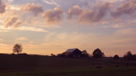 KENTUCKY - CIRCA 2020s - Clouds drift above a beautiful barn and horses grazing in rural Kentucky.