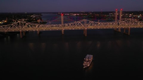 JEFFERSONVILLE, INDIANA - CIRCA 2020s - Night aerial of bridges and paddlewheel boat on the Ohio River.