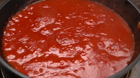 Tomato soup is boiling in a pan. Boiling bubbles on tomato sauce. Close up, top view, macro food, 4K. 