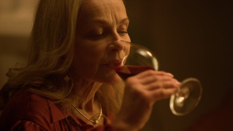 Thoughtful old aged woman drinking red wine glass at restaurant date. Closeup melancholy mature lady tasting alcohol drink indoors. Sad grandmother wife thinking about upset retirement life concept