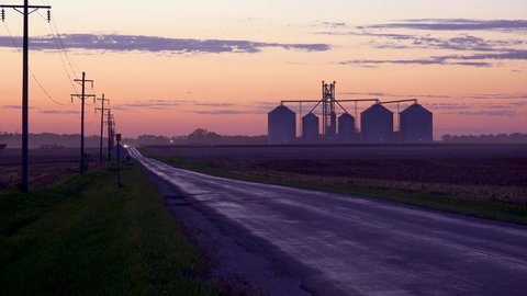 AMERICAN MIDWEST - CIRCA 2020s - Grain silos on a large commercial farm along a country road at dusk in the Midwest.