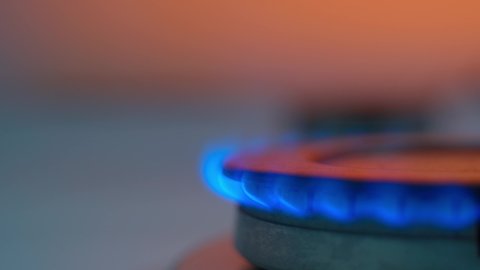 Kitchen burner turning on, close up, copy space, turns off. Natural gas inflammation, close up. Stove burner lights up and burns with a blue flame on an orange background.