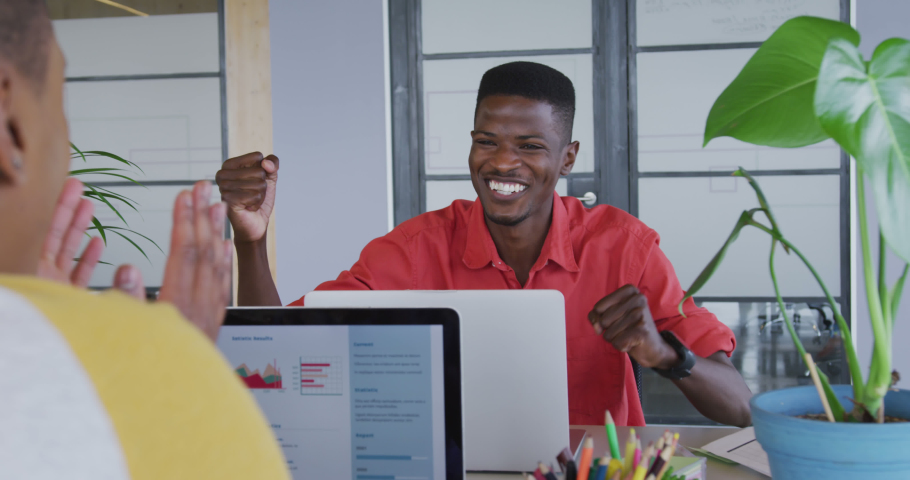 Happy african american creative businessman high fiving with female colleague at desk in office. business and technology in office workplace.