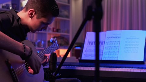 Cinematic footage of teenager plays guitar in his room. Young man plays a musical instrument. Musician records his composition in a music Studio using professional microphone. Professional lighting 