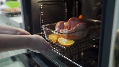 Woman putting whole chicken in the oven in modern kitchen, making roasted chicken baked in the oven. High quality 4k footage