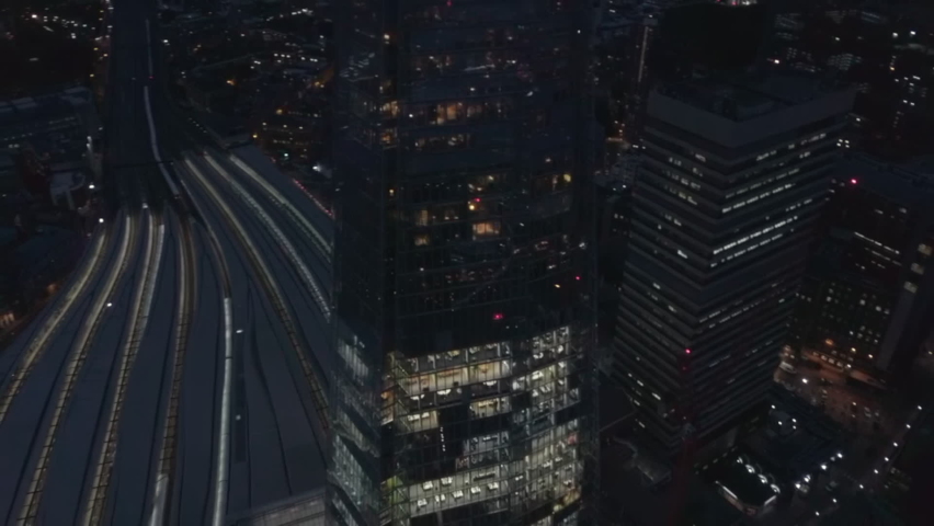 Scenic aerial view of London Bridge Tower, The Shard at night. Drone tilt down, circling around illuminated skyscraper, tilt up reveal spectacular London cityscape