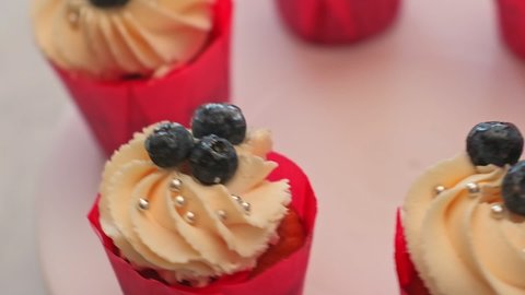 Delicious cupcakes decorated with blueberries and beads spin on the pastry platform, top view