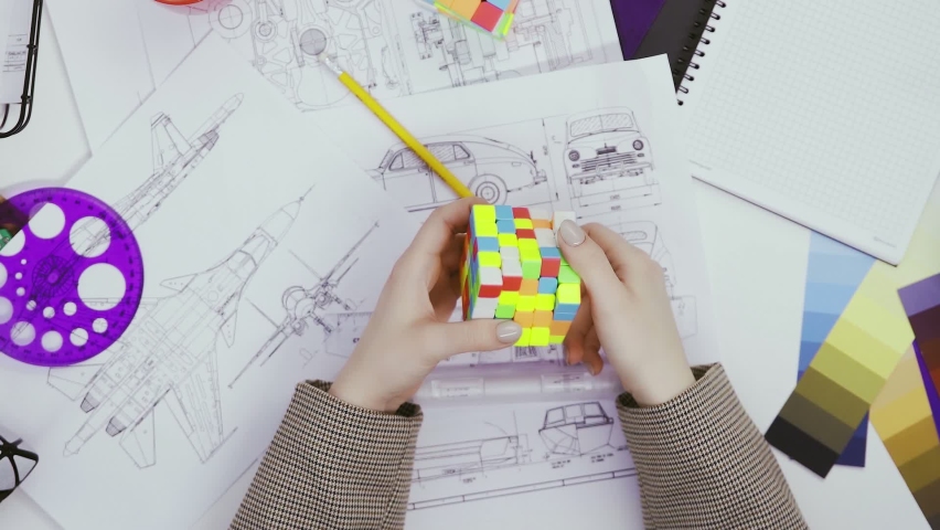 Top view the hands of a female designer solve a puzzle with a Rubik's cube. Cube puzzle, a puzzle game.