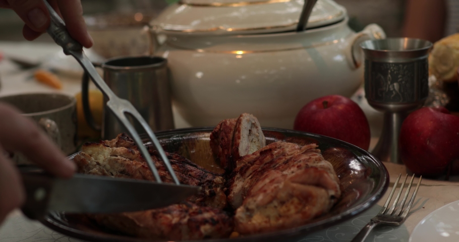 POV hands serve and cut stuffed turkey roll using knife and two prong fork on Thanksgiving dinner table with vintage crockery. Traditional Thanksgiving turkey roulade roasted on grill. Serving dinner