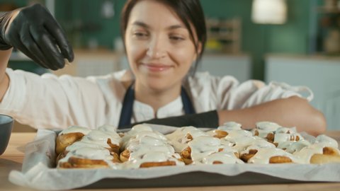 Close-up. A Contented Female Pastry Chef Sprinkles Almonds on the Glazed Buns. Cinnabones. Sweet Cream Cheese Frosting on Cinnamon Rolls. Pastry Baked Goods and Favorite Business.
