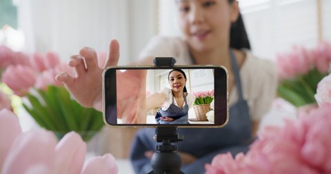 Asia young girl vlogger influencer or SME owner people smile work on home selfie shoot filming live sell show happy talk on mobile screen VoIP app. Remote sale product at modern florist gift shop.
