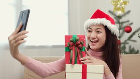 Cute asian girl in christmas holiday holding gift box using smartphone video call to family. Happy beautiful Asian women celebrate with present gift box in christmas party and shared to social