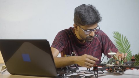 Handheld shot of student checking quadcopter or drone by connecting to laptop at home laboratory - concept of UAV developing, Repairing or Experimenting