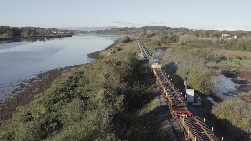 Following aerial of freight train hauling railroad tracks along river