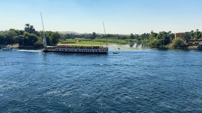 Cinematic video of a large Egyptian cruise boat sailing along the banks of the green Nile River Valley during a vacation. Concepts of tourism industry and travel to Egypt.