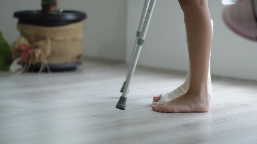 Young woman with broken leg in plaster cast trying to walk with crutches in living-room. Physical injury, bone fracture and accident, Royalty-Free Stock Footage #1081896563